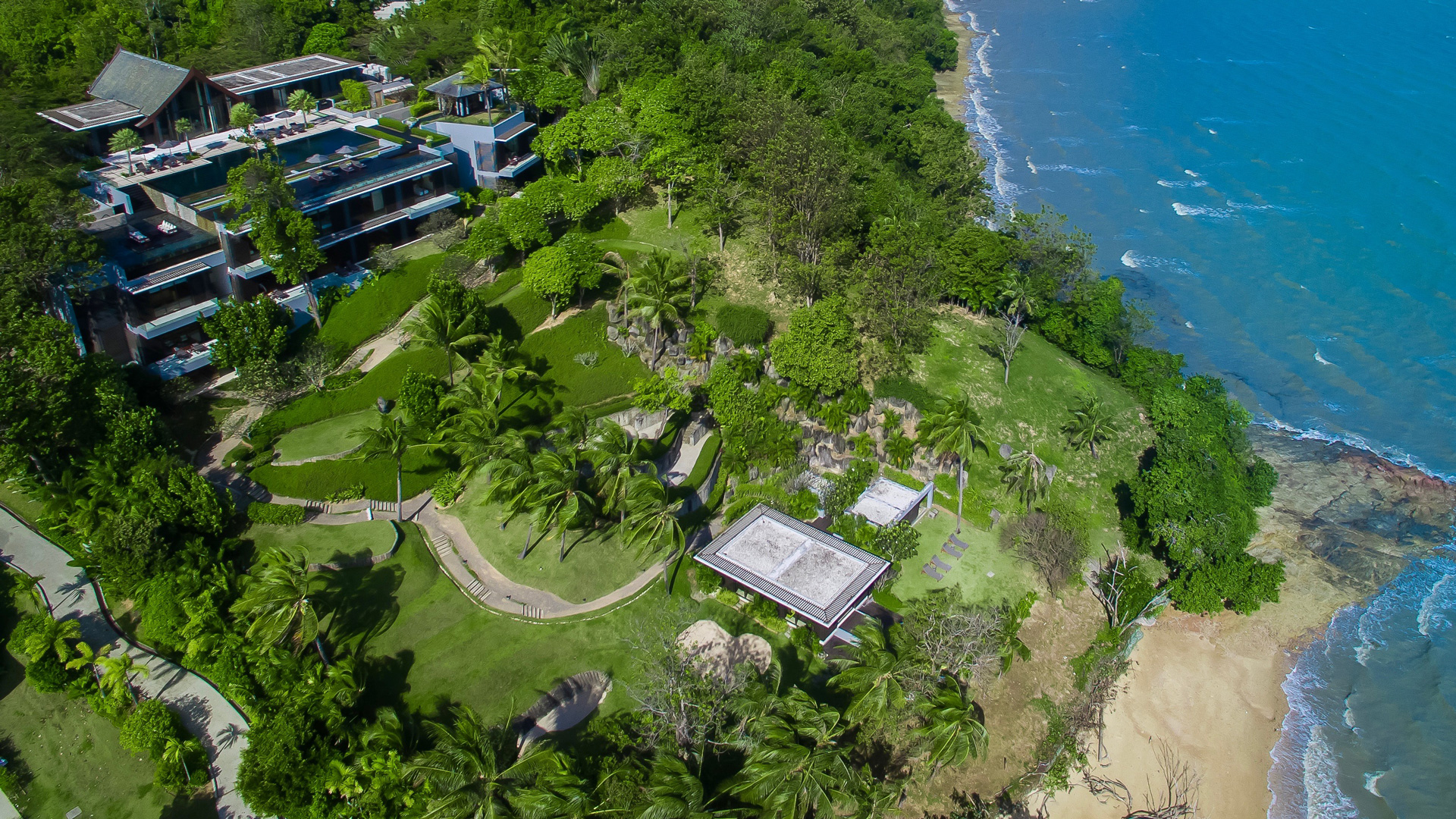 Villa Sawarin from above: pavilions and terraces stepping down a green headland to a lone beach house and the sea.